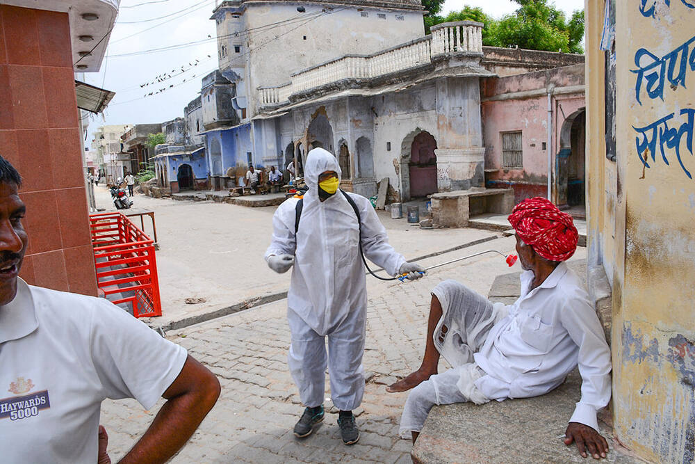 Worker in PPE spraying disinfectant on a village street, Ralawata