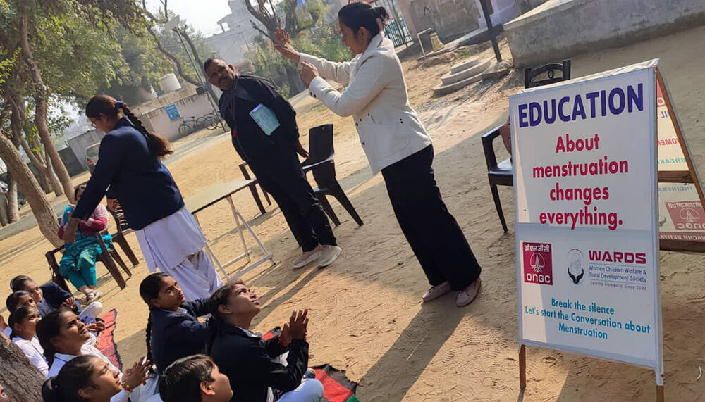 Outdoor school session, 'Education about menstruation changes everything' signage, Village Pahari