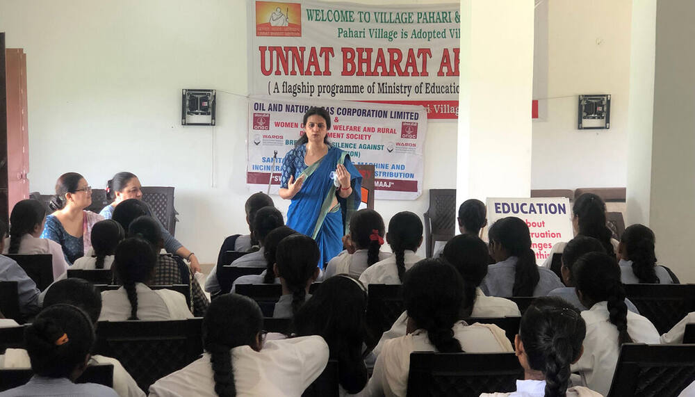 Indoor hall session, Unnat Bharat Abhiyan banner naming Village Pahari