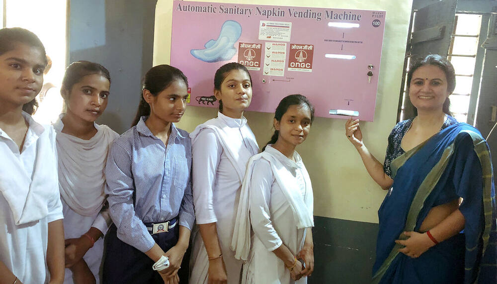Sanitary napkin vending machine installed on campus, with students and Dr. Shweta Laddha, Village Pahari
