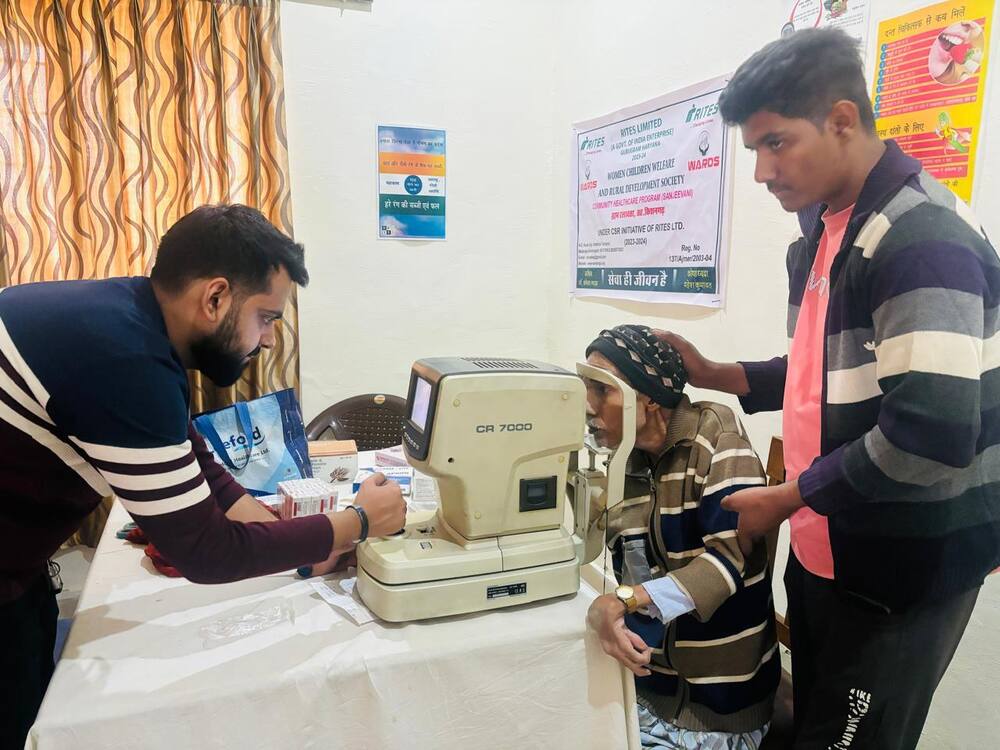 Optometrist examining an elderly patient with an autorefractor, RITES-WARDS Sanjeevani banner